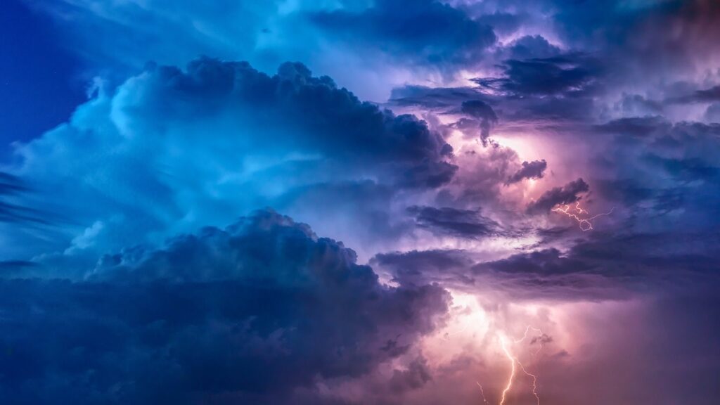 Das Bild zeigt dunkelblaue Wolken und einen hellen Blitz, der aus dem Himmel auf die Erde trifft.
